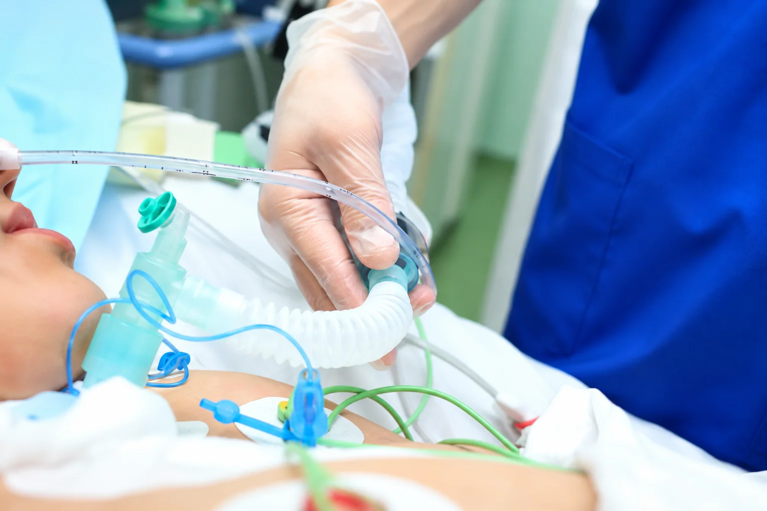 Healthcare professional providing respiratory care to a patient using medical equipment in a clinical setting.
